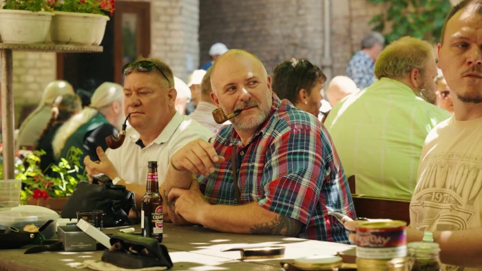 Group of friends cheerfully chatting and smoking pipes at tables